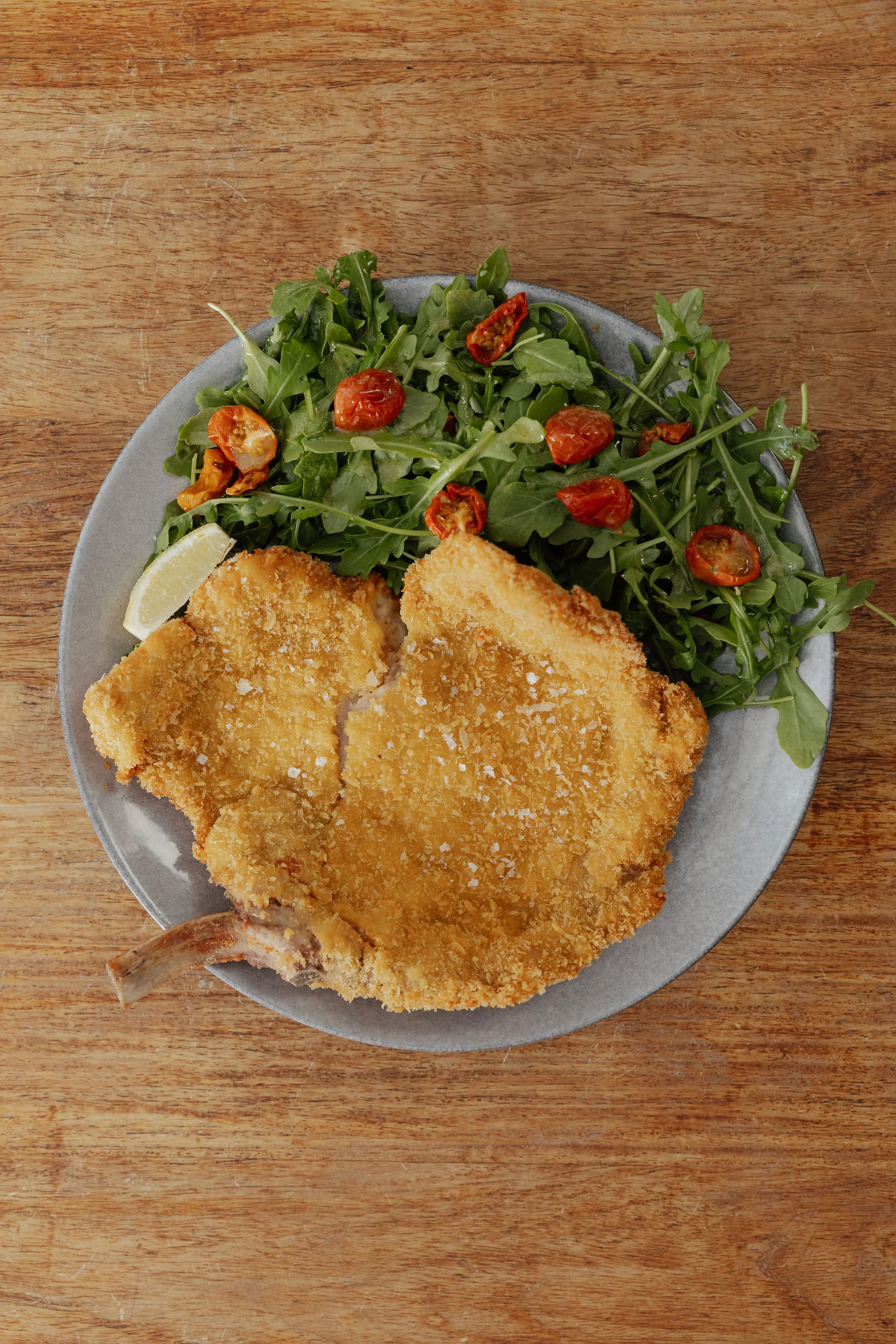 Golden cotoletta with rocket, tomatoes and lemon